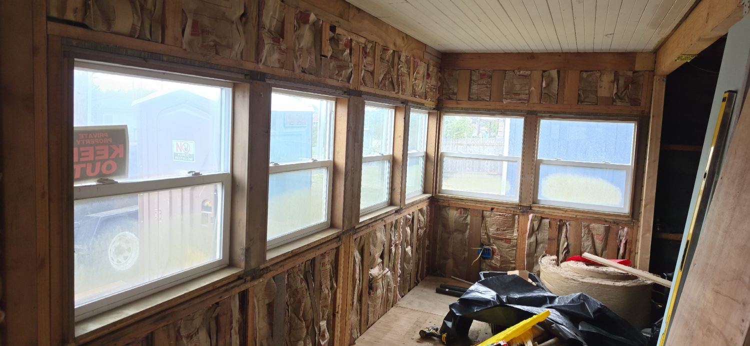 Sun porch opened to the studs, old insulation showing, windows along two walls